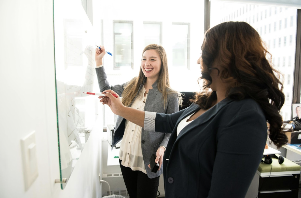 2 Women Standing in Front of a Whiteboard